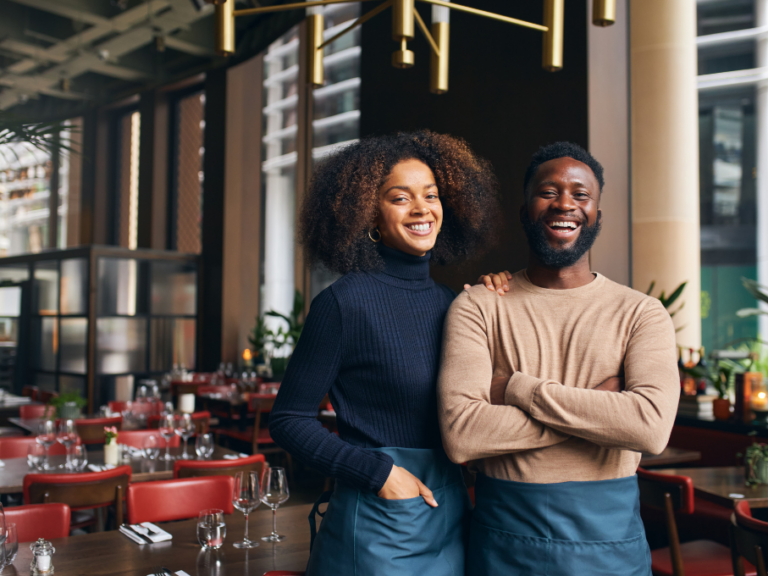 Male and female restaurant owners standing in the dining room, smiling.