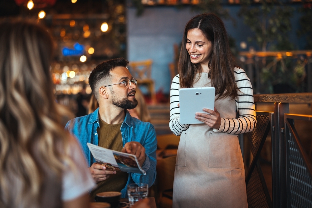 A waitress takes an order from a guest holding a menu