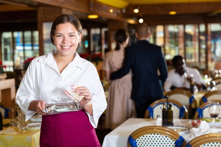 Cheerful young waitress standing with money in restaurant and smiling