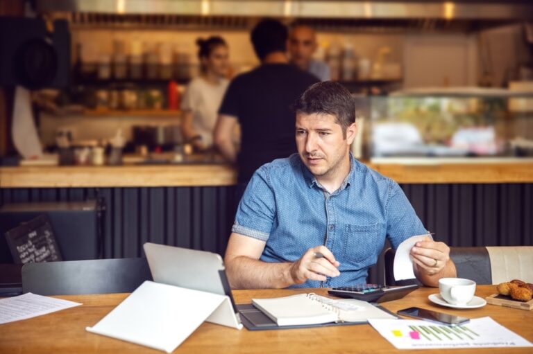 Small business owner sitting in restaurant with a laptop working on restaurant accounting.