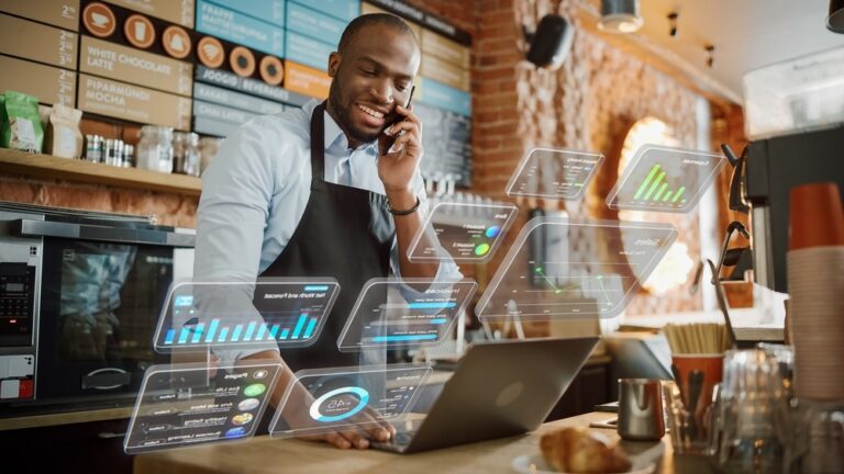 Coffee shop manager works on a computer and talks on a phone in a cafe