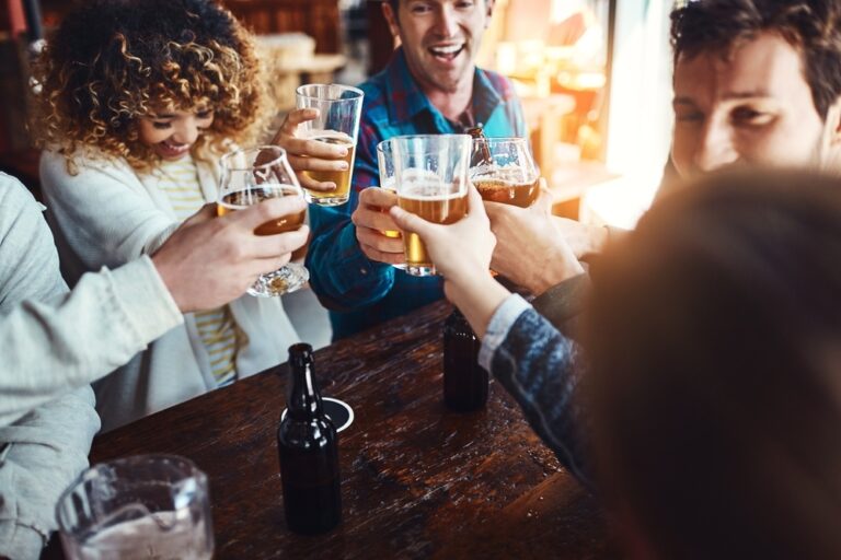 Happy friends laughing and toasting with beers at restaurant