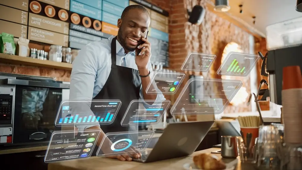 Coffee shop manager works on a computer and talks on a phone in a cafe
