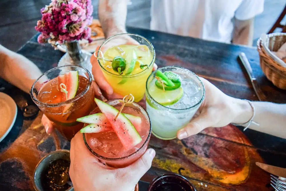 Friends toasting, saying cheers holding tropical blended fruit margaritas