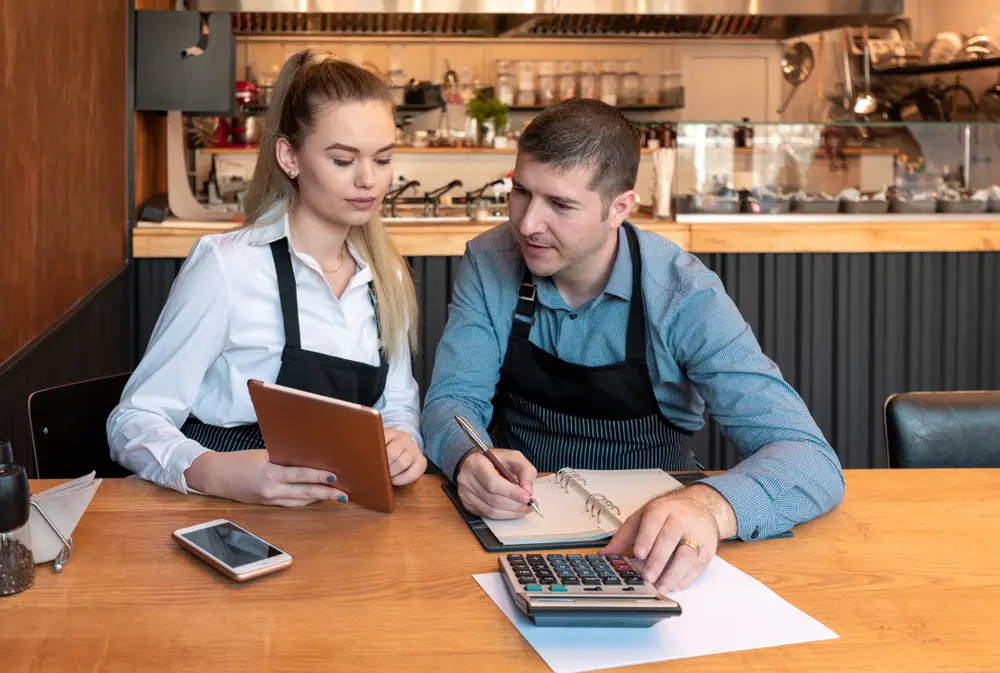 Woman and man doing restaurant accounting with calculator