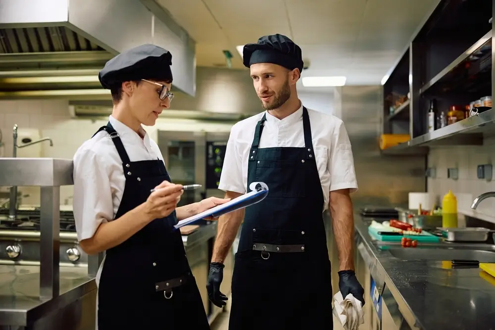 Two cooks review a checklist in the restaurant kitchen