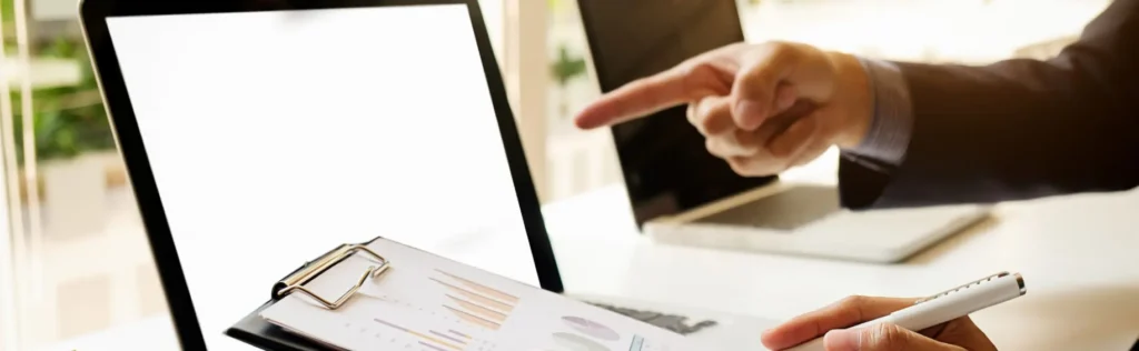 Male finger pointing towards laptop screen, clipboard with metrics in foreground.