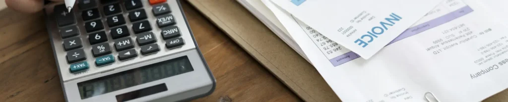 Calculator, pen, and invoices on a desk.