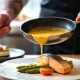 Chef pouring sauce over plated salmon with vegetables, demonstrating controlled portion size