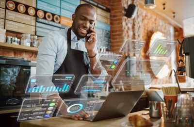 Coffee shop manager works on a computer and talks on a phone in a cafe