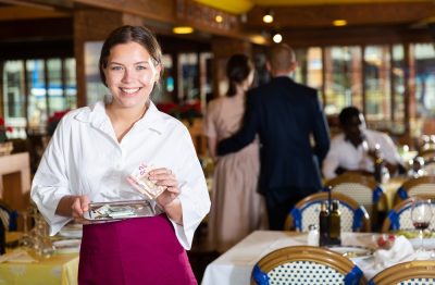 Cheerful young waitress standing with money in restaurant and smiling