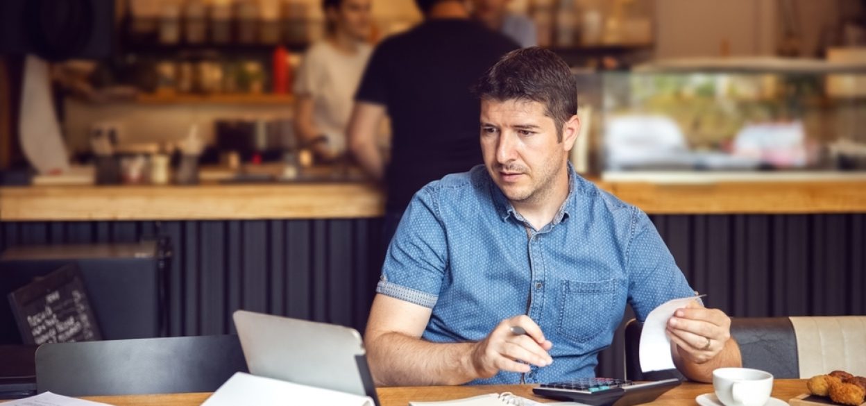 Small business owner sitting in restaurant with a laptop working on restaurant accounting.