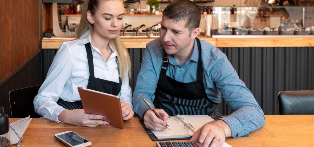 Woman and man doing restaurant accounting with calculator